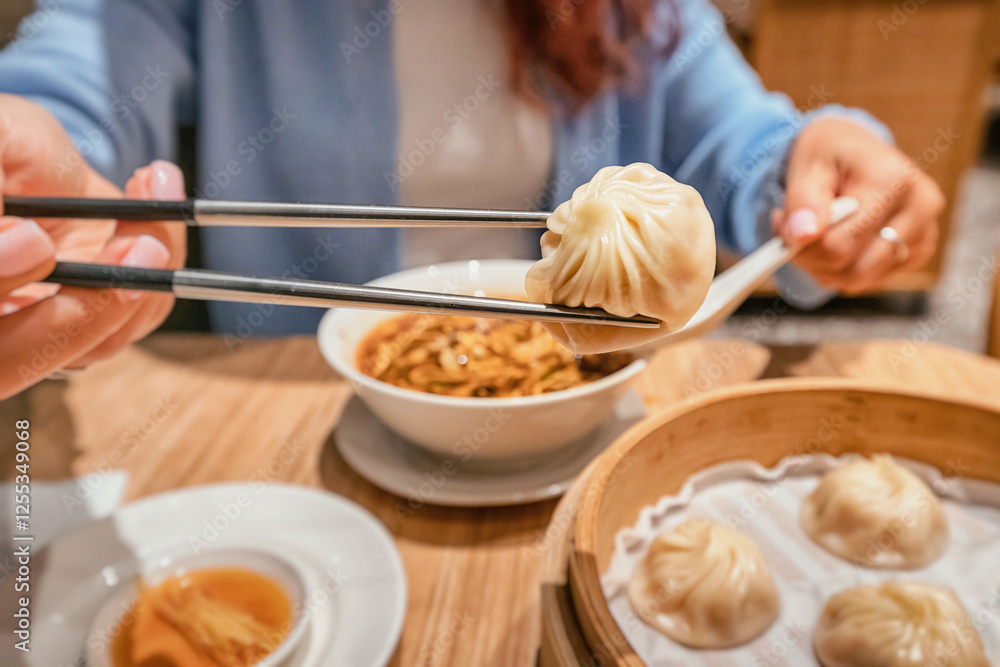Close up of woman using chopsticks picking up a xiaolongbao dumpling from bamboo steamer basket in a chinese restaurant