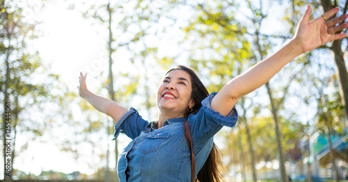 Happy woman in a denim shirt enjoying nature with arms wide open