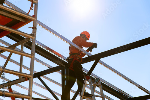 Construction worker using drill machine on metal scaffold under sky photo