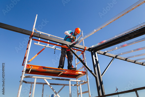 Mature construction worker installing metal tubes with drill under blue sky