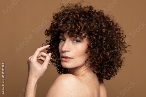 Sensuous woman looking over shoulder against brown background photo