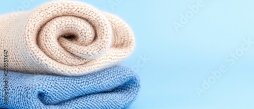 Rolled Beige and Blue Knit Sweaters on Light Blue Background