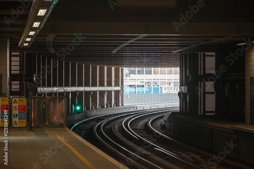 A dimly lit overground train station in London with curved tracks leading towards an opening photo