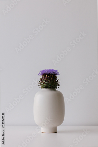 Artichoke in full bloom with purple flower in a white vase.