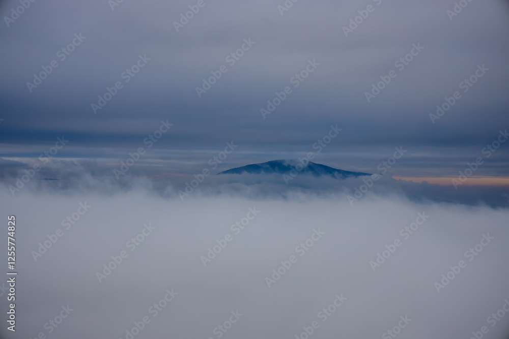 Obraz premium Winter cloudscape mountains view. Fog and mist on the sky with some dark clouds in a freezing morning air among the mountains and hills in Brasov, Romania