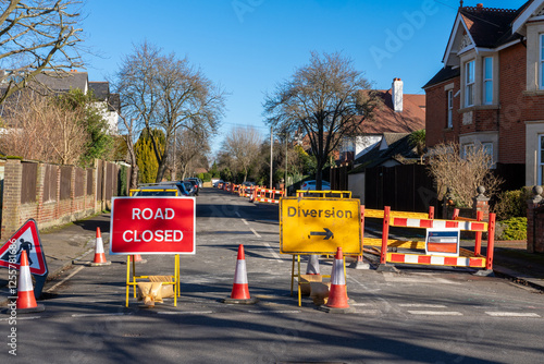 Signs of road closed and diversion with cones and barricade on road quiet urban street sunny day photo