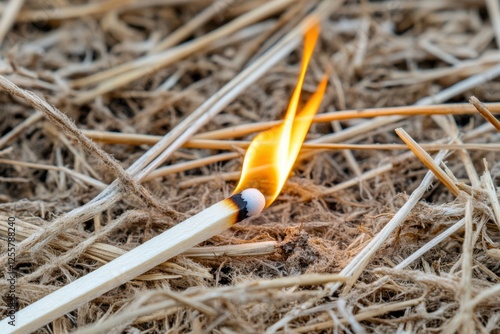 Burning matchstick igniting on dry hay, creating a small flame on the ground.