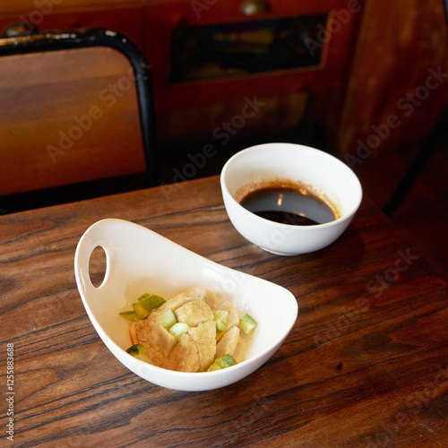 Indonesian traditional pempek, A small white bowl filled with pempek and garnished with green slices sits next to a bowl of dark dipping sauce on a wooden table photo