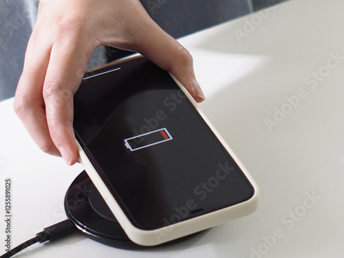 Charging mobile phone battery with wireless charging device in the table. Smartphone charging on a charging pad. Mobile phone near wireless charging