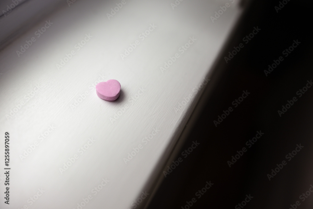 close-up of a single isolated pink pastel Valentine's Day candy heart on a white wooden window sill in natural light close-up of a single isolated pink pastel Valentine's Day candy heart on a white wooden window sill in natural light