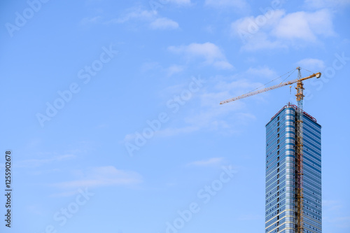 Construction tower crane on construction site near tall glass building against sky. Construction crane builds high-rise residential building. High-rise construction concept, apartment building. photo