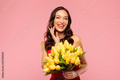 Young pretty woman in dress smiling tenderly, holding bouquet of yellow tulips against pink background. 8th of March and International Women's Day gift photo