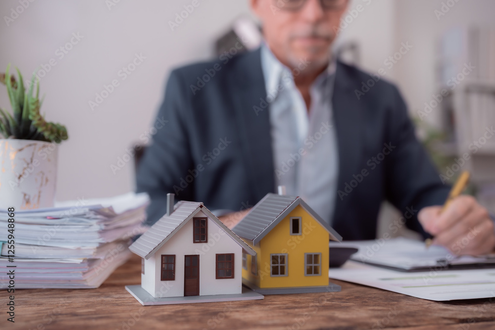 Miniature houses are on the wooden desk of a real estate agent calculating the investment for buying property, with documents and calculator Miniature houses are on the wooden desk of a real estate agent calculating the investment for buying property, with documents and calculator