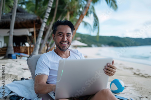 Cheerful businessman works on his laptop confidently while relaxing on a vibrant, sunlit beach photo