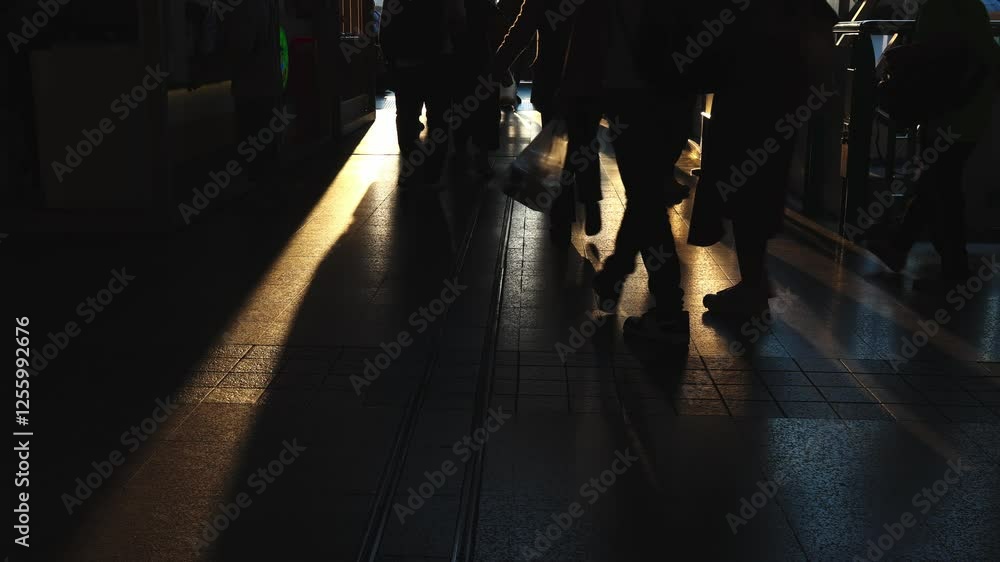 Silhouette of crowd people walking against sunset light. Shadows of busy pedestrians walking after work through a golden sunset on a train station. Long shadows and warm lights of evening atmosphere. Silhouette of crowd people walking against sunset light. Shadows of busy pedestrians walking after work through a golden sunset on a train station. Long shadows and warm lights of evening atmosphere.