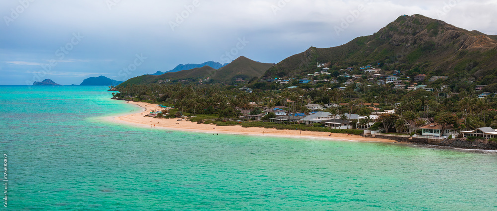 Obraz premium Aerial view of Oahu, Hawaii, showing a sandy beach, turquoise waters, residential homes, lush greenery, rolling hills, and distant islets.