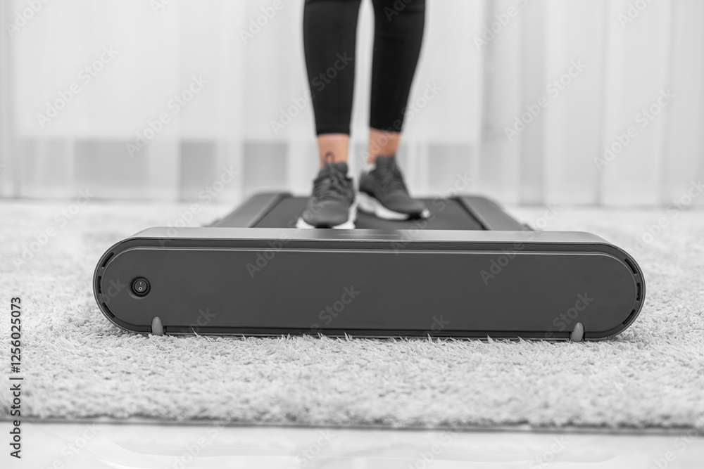 A person wearing black leggings and gray sneakers is walking on a compact treadmill in a modern, minimalistic home environment, focusing on fitness and an active lifestyle.