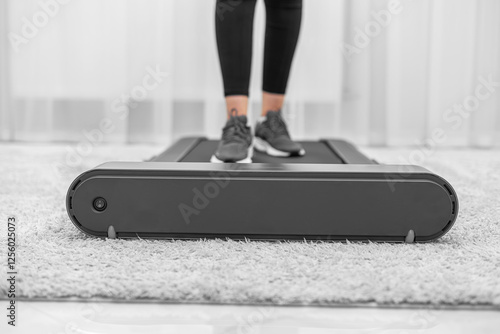 Obraz na płótnie A person wearing black leggings and gray sneakers is walking on a compact treadmill in a modern, minimalistic home environment, focusing on fitness and an active lifestyle. w salonie