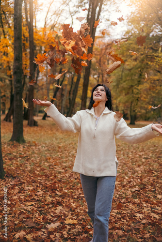 Joyful woman enjoying autumn leaves in scenic forest photo