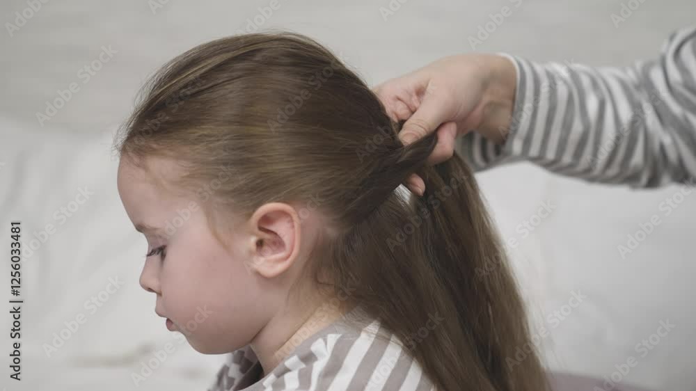 Mother braids child long brown hair. Mom creates hairstyle daughter brunette loose hair. Mum and preschooler girl take care hair closeup slow motion. Happy family. Mom kid together happy family indoor Mother braids child long brown hair. Mom creates hairstyle daughter brunette loose hair. Mum and preschooler girl take care hair closeup slow motion. Happy family. Mom kid together happy family indoor