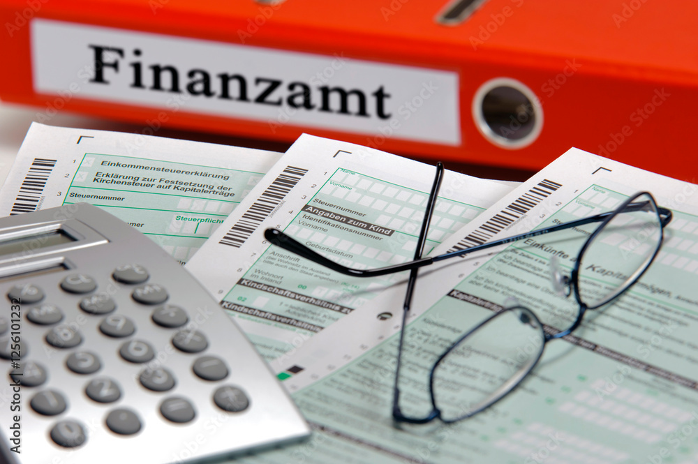 Φωτογραφία Vor einem Aktenordner mit Beschriftung Finanzamt liegen Formulare für die Steuer