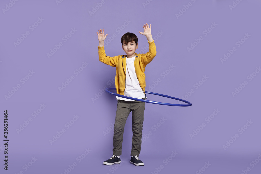 Fototapeta premium Boy exercising with hula hoop on violet background
