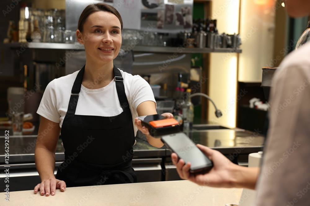 Cafe worker taking payment from client via terminal indoors Cafe worker taking payment from client via terminal indoors