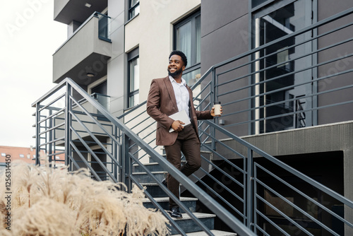 Happy interracial businessman walking down the stairs with tablet and coffee to go in hands at financial district.