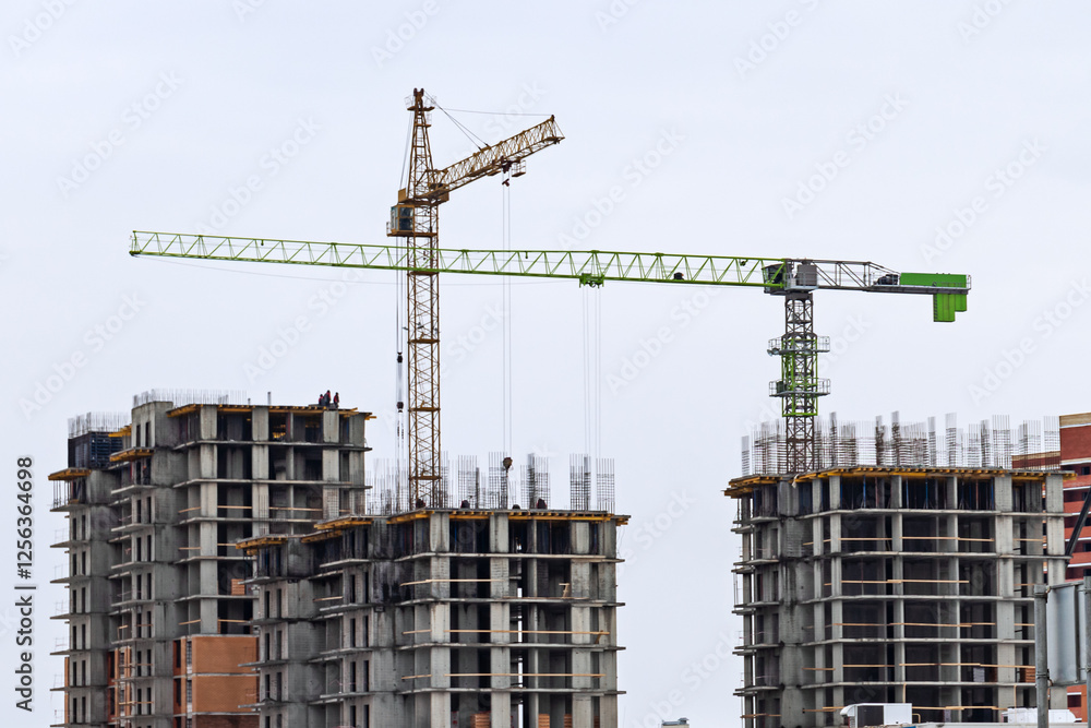 Construction site with cranes assembling concrete structures under overcast sky, urban development in progress Construction site with cranes assembling concrete structures under overcast sky, urban development in progress