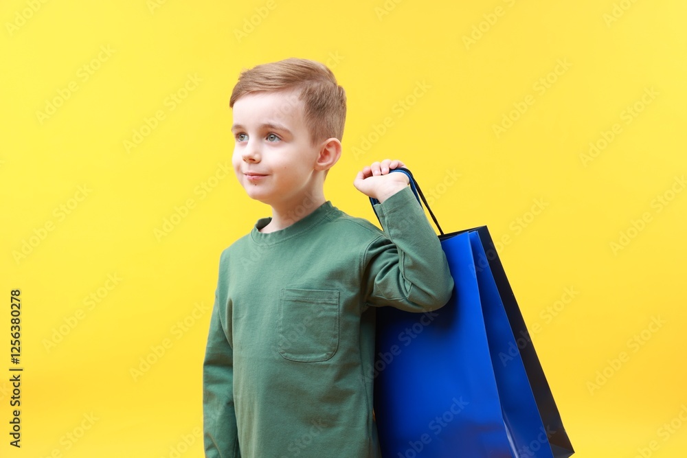 Cute little boy with shopping bags on yellow background Cute little boy with shopping bags on yellow background