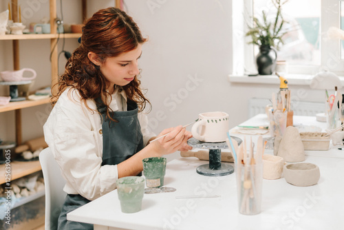 Process of designing cup with a traditional pattern in pottery art studio. Artisan stamps decorative symbols on the dry clay of the cup. photo