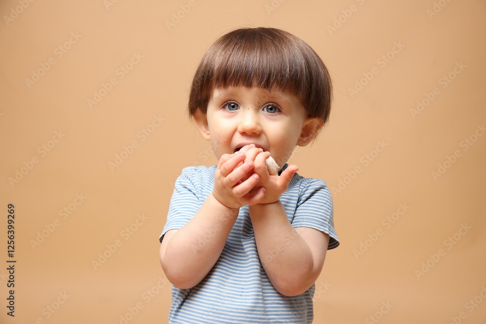Cute little child eating tasty mochi on light brown background Cute little child eating tasty mochi on light brown background