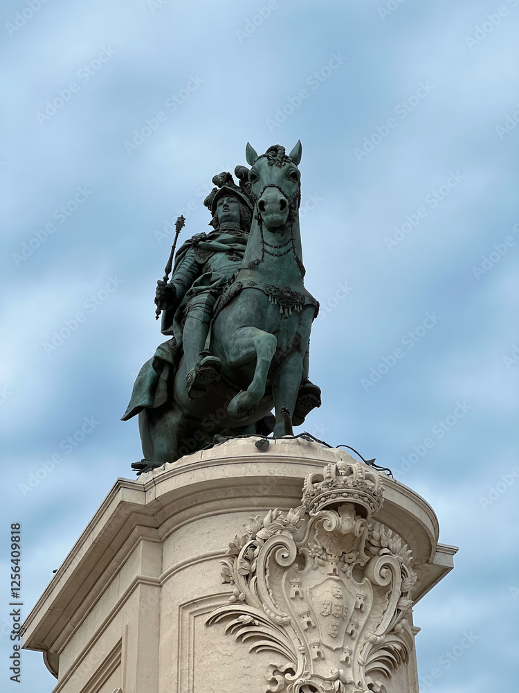 Obraz premium Description (under 200 characters):Low angle shot of the Equestrian Statue of King José I in Lisbon, Portugal, against a cloudy sky. Detailed sculpture atop a decorated arch, showcasing historical
