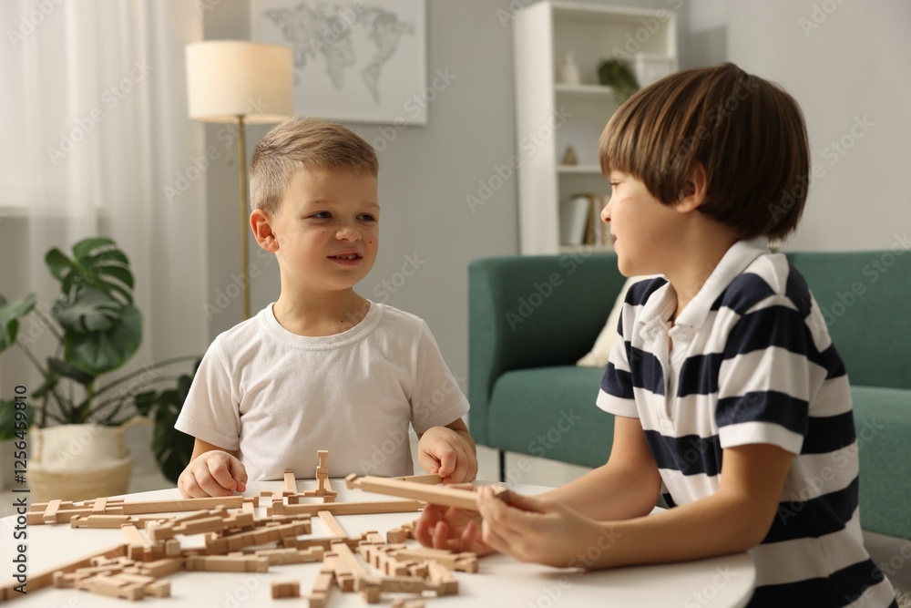 Fototapeta premium Cute brothers playing with wooden construction set at table indoors