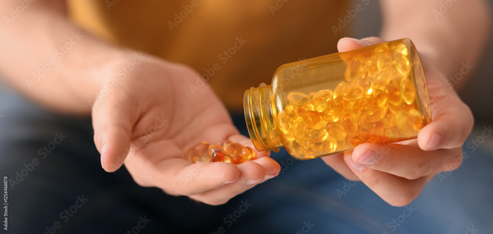 Handsome young man with jar of fish oil capsules at home, closeup Handsome young man with jar of fish oil capsules at home, closeup