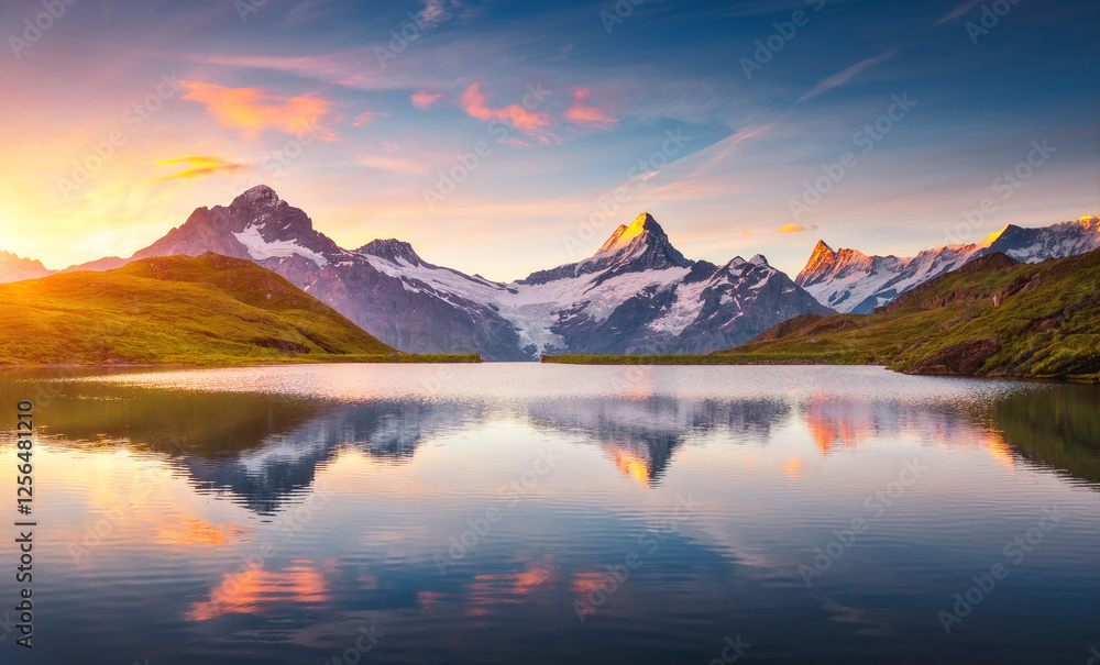 A high snow-capped rocky massif is reflected in Lake Bachalpsee at sunset. Location place Bernese Alps, Grindelwald valley, Europe. A high snow-capped rocky massif is reflected in Lake Bachalpsee at sunset. Location place Bernese Alps, Grindelwald valley, Europe.