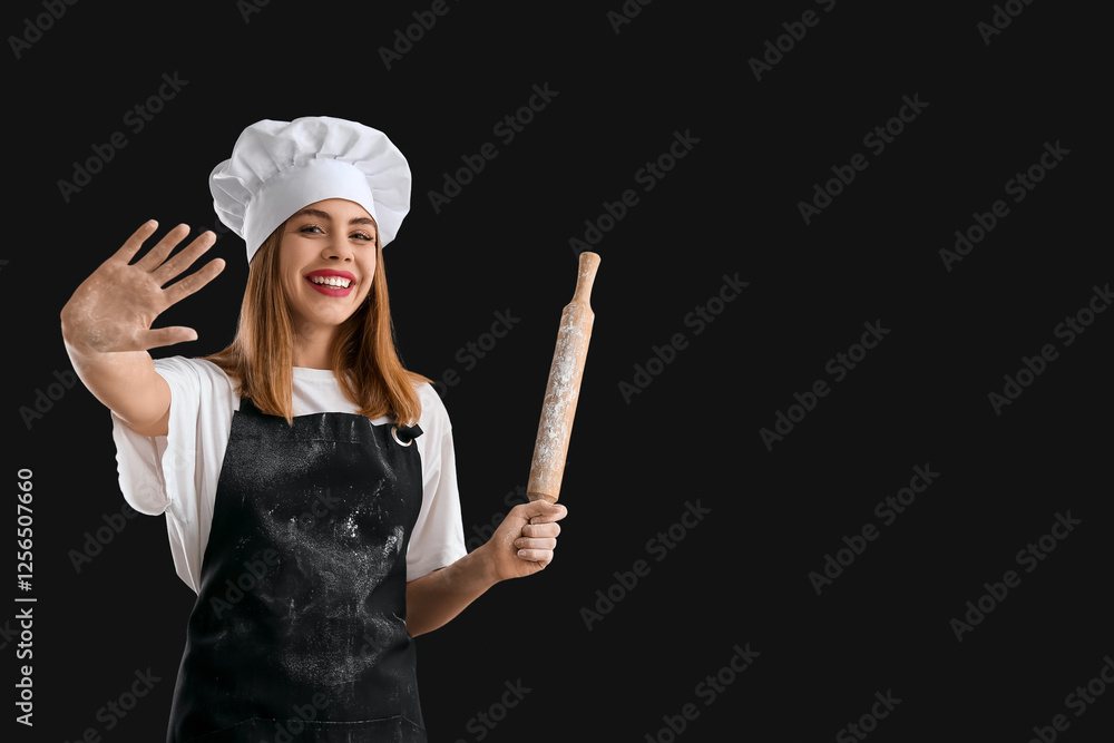 Young female chef with rolling pin and flour stains on black background