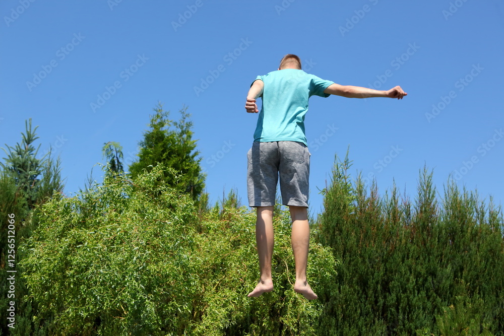 A boy is joyfully jumping high into the air over trees beneath a brilliantly clear sky A boy is joyfully jumping high into the air over trees beneath a brilliantly clear sky