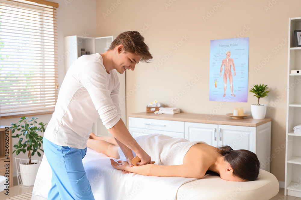 Obraz premium Male therapist massaging young woman's arm with wooden scraper in spa salon