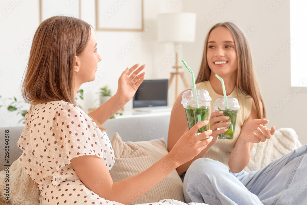 Beautiful young happy women with glasses of mojito sitting on sofa at home Beautiful young happy women with glasses of mojito sitting on sofa at home