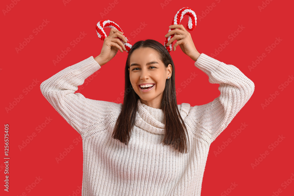Happy young woman with Christmas candy cane toys on red background Happy young woman with Christmas candy cane toys on red background