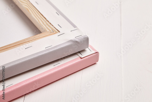 Close-up of the backside of two stacked photo canvas prints, one pink and one gray, showcasing tightly stretched corners, staple details, and wooden frames on a white surface photo