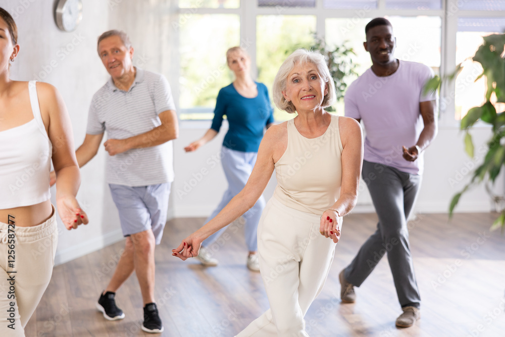 Smiling senior woman visiting group choreography class with adult people of different ages, learning modern dynamic dances. Concept of active lifestyle