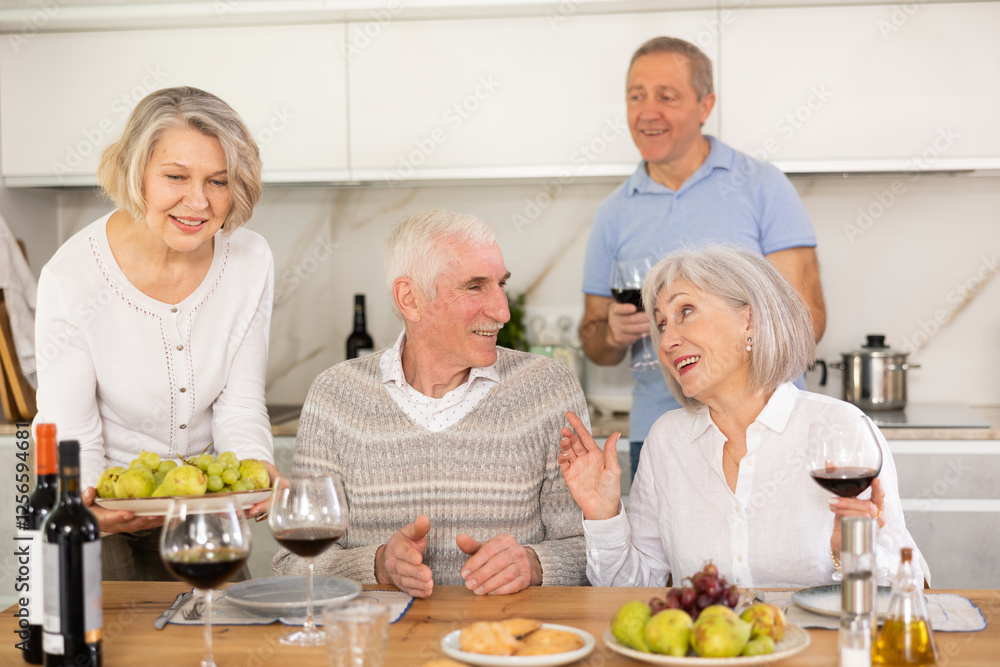 During friendly gatherings in kitchen, elderly woman sets table, serves large plate of fruit, treats elderly friends. During friendly gatherings in kitchen, elderly woman sets table, serves large plate of fruit, treats elderly friends.