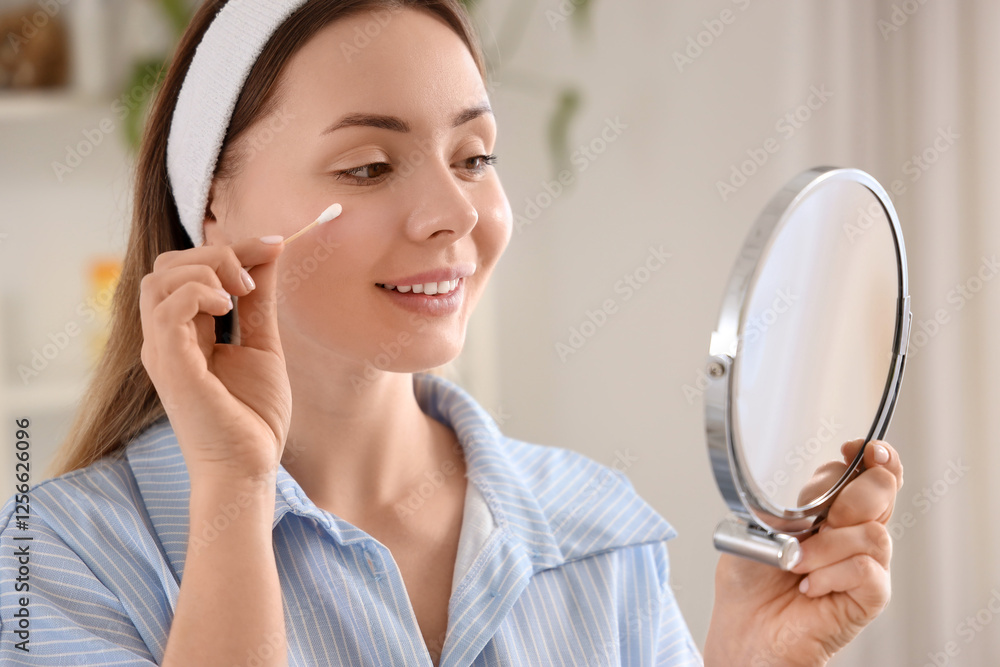 Young woman cleaning face with cotton bud and mirror in bathroom, closeup Young woman cleaning face with cotton bud and mirror in bathroom, closeup