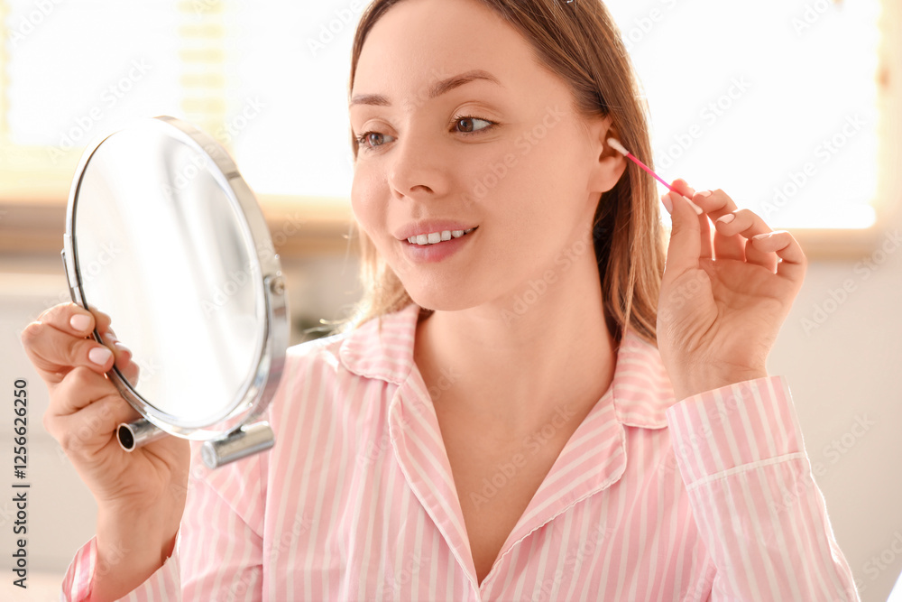 Young woman cleaning ears with cotton bud and mirror in bedroom, closeup Young woman cleaning ears with cotton bud and mirror in bedroom, closeup