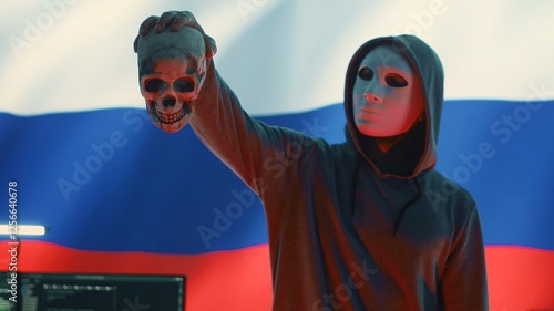 Russian cyber criminal with anonymous mask and hood holding a skull, making death threats and asking for ransom. Dangerous evil person symbolizing cyber threats and cyberterrorism. Camera A. photo