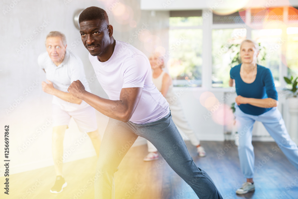 Fototapeta premium Energetic African American man practicing hip-hop movements during adult group dance class in studio