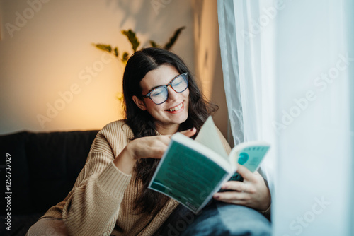 Foto Young caucasian woman reading book or learning by the window