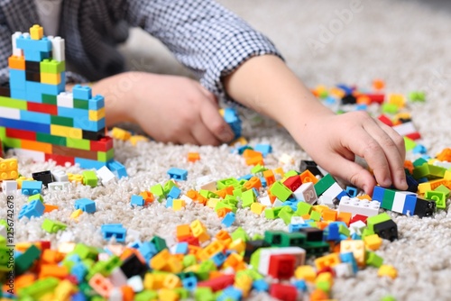 Cute boy playing with building blocks on floor at home, closeup